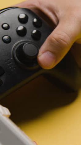 Vertical-Video-Close-Up-Hand-Picking-Up-Video-Game-Controllers-Yellow-Background